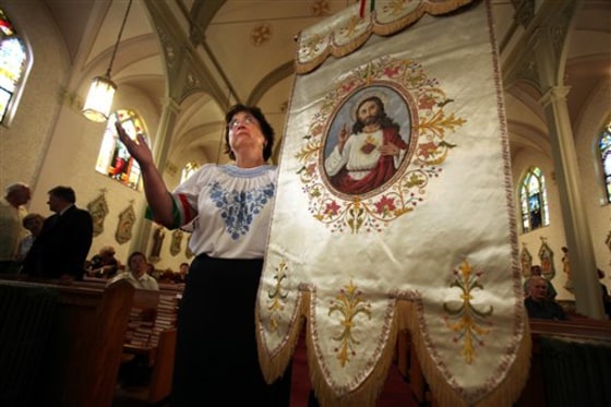 Elizabeth Beresh, a parishioner at the closed Sacred Heart of Akron, holds a banner from her church as she prays at the altar of St. Emeric's Church on Wednesday. Bishop Richard Lennon was supposed to conduct the final service at the church but canceled it.